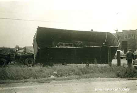Pictured is an overturned truck at Elmer Brewer Trucking Co. Building visible in background.