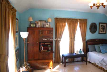 View of bedroom showing wooden wardrobe with drop-down desk shelf, sitting bench and typical lighting fixtures.