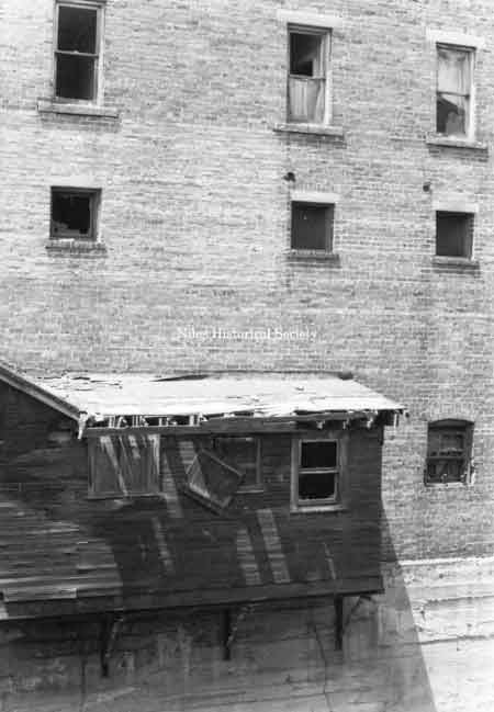 Photo taken of rear fa&ccedil;ade of building overhanging Mosquito Creek showing marked deterioration.